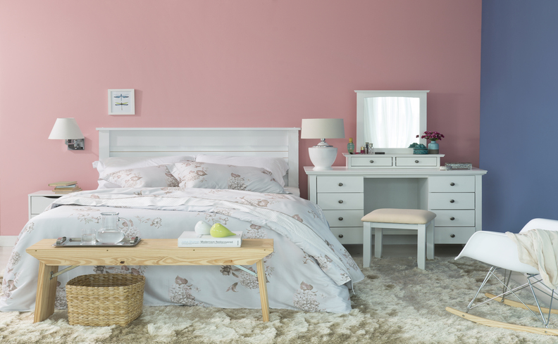 tipos de dores nas costas, quarto com cama de casal com edredom branco com estampas florais, dois travesseiros, banco nos pés da cama, penteadeira e banquinho.