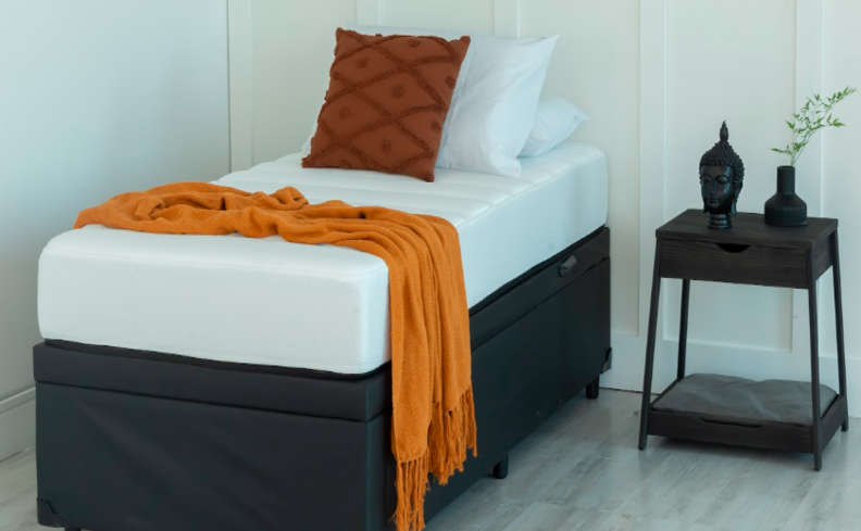 um quarto com colchão novo em uma cama de solteiro, com travesseiros, almofadas e manta