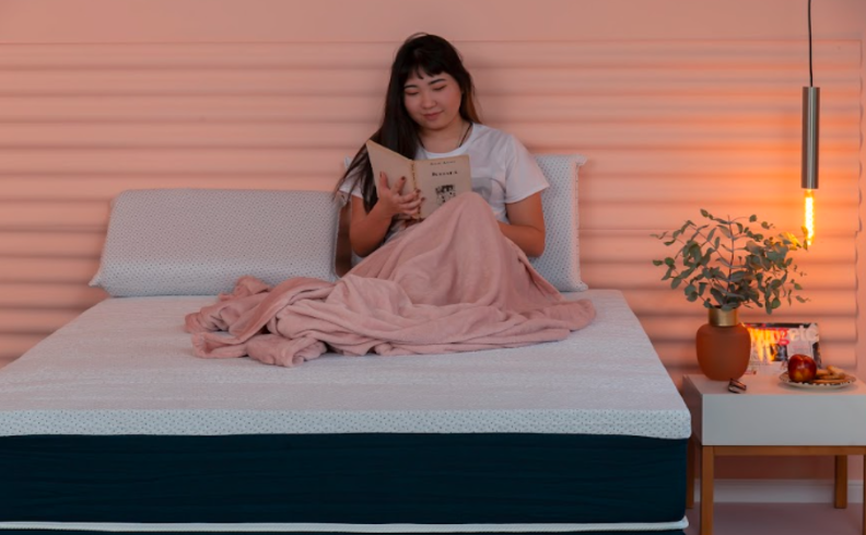 mulher sentada em uma cama com cobertor e travesseiros lendo um livro após ter uma noite mal dormida