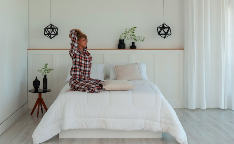 mulher sentada em uma cama se perguntando o que um colchão ruim pode causar após ter uma noite de sono ruim