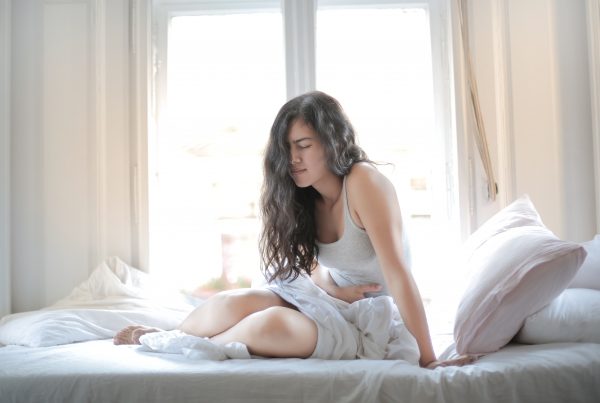 Perigos que um colchão ruim pode trazer para sua saúde, com mulher sentada na cama com dores.