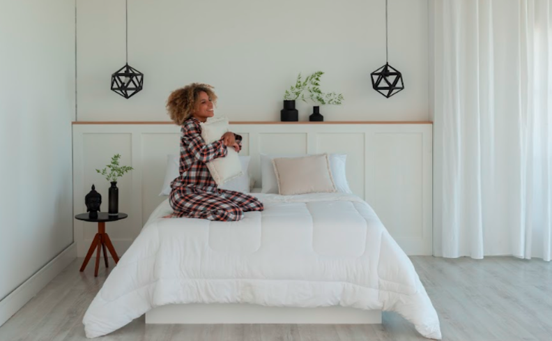 colchão que vem dobrado em um quarto com roupa de cama branca, travesseiros, pendentes, mesa de cabeceira e itens decorativos