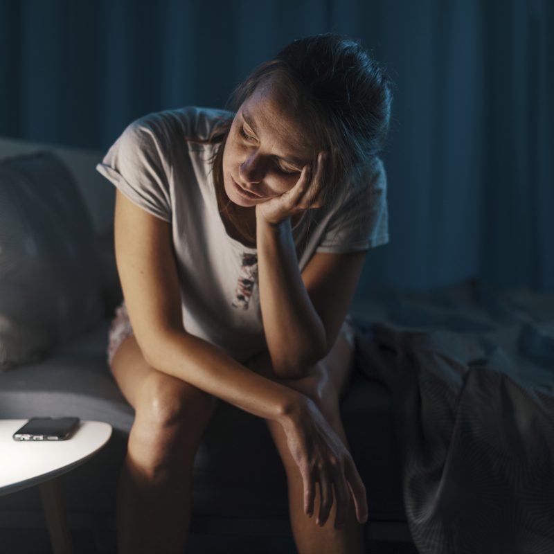 mulher sentada na cama tentando entender o que causa insônia