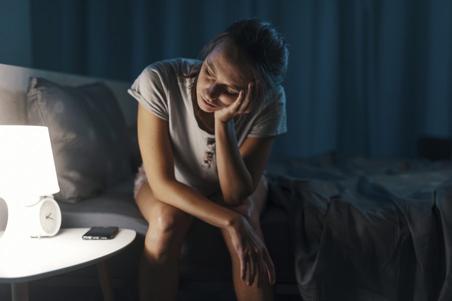 mulher sentada na cama tentando entender o que causa insônia