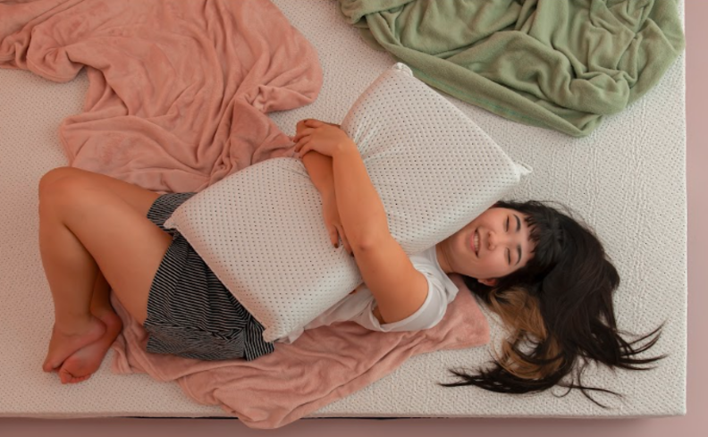 como parar de roncar, mulher deitada abraçando um travesseiro em uma cama com dois cobertores