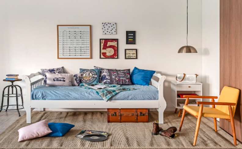 como limpar colchão em casa em um quarto com cama de solteiro bagunçada com roupa de cama azul, diversas almofadas, poltrona amarela, tapete, mesa de apoio e itens decorativos.