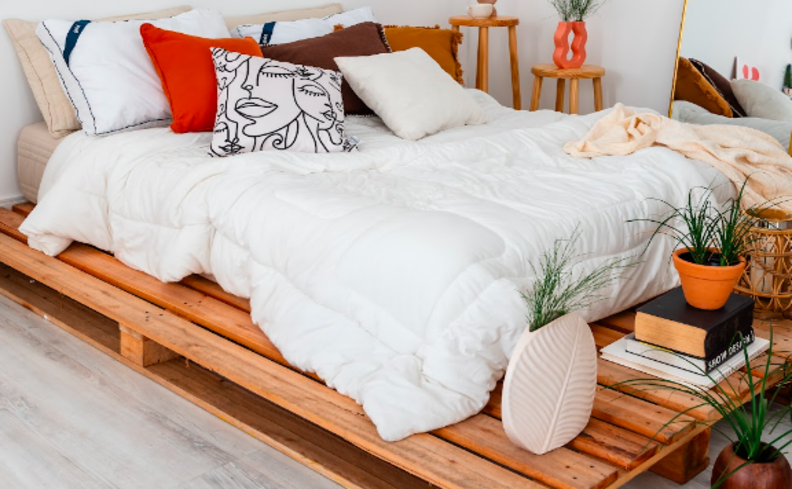 como tirar mancha do colchão em um quarto com colchão de casal no estrado, diversas almofadas, travesseiros e vasos com plantas.