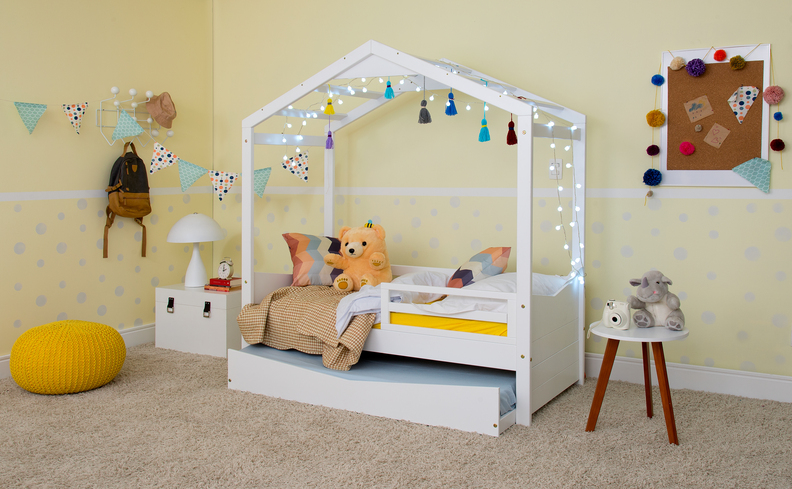 quarto infantil com cama, colchão para criança, mesa lateral, puff, luminária de mesa e diversos itens decorativos