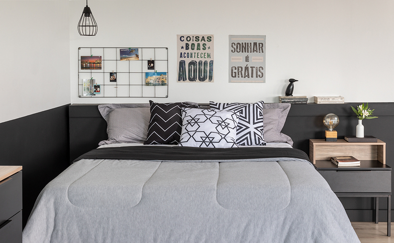 quarto casal completo com cama, colchão, roupas de cama cinza e preta, almofadas e travesseiros, além de quadros decorativos e mesa de cabeceira