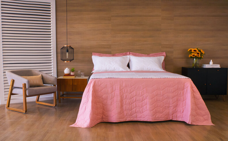 quarto com travesseiro hipoalergênico, roupa de cama rosa, poltrona, mesas de cabeceira e lustre pendente