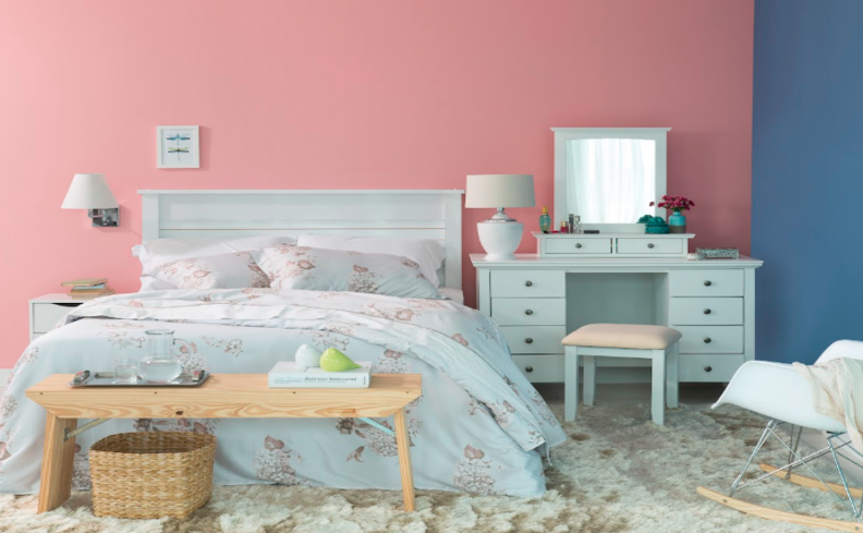 quarto com travesseiros nasa, roupa de cama azul com flores, peseira, penteadeira e banqueta
