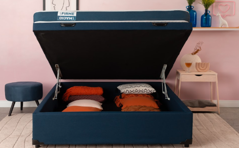 base de cama baú casal aberta com almofadas e diversas roupas de cama guardadas no interior para otimizar o espaço.