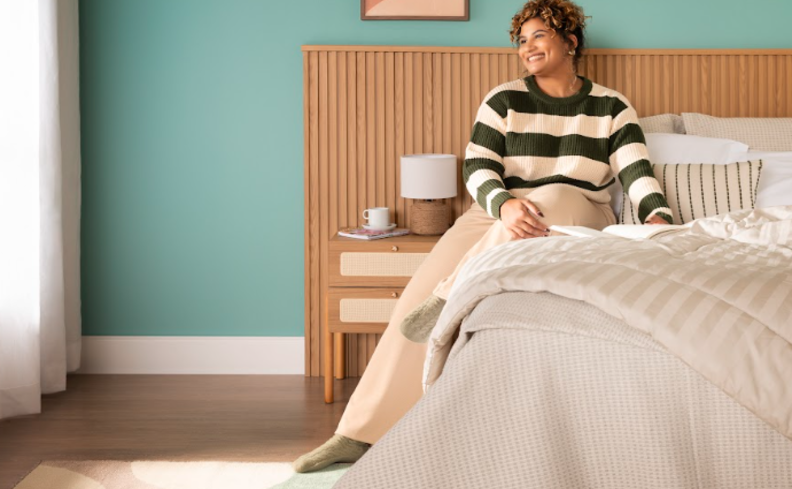 ficar sem dormir faz mal com uma pessoa sentada na cama em um quarto com cama, cabeceira, mesa de cabeceira e itens decorativos
