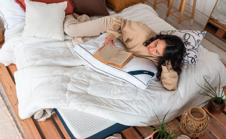 dormir mal engorda, pessoa deitada na cama lendo um livro com cobertores, travesseiros e itens decorativos no ambiente