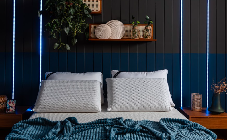 colchão macio em um quarto com cama, travesseiros, mesa de cabeceira com itens decorativos.