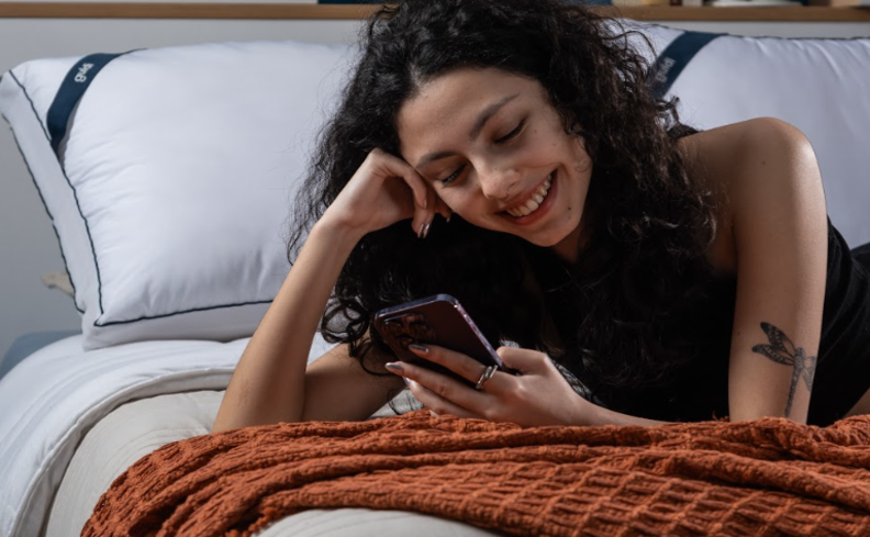 mulher deitada de bruços na cama segurando um celular pesquisando o que faz a pessoa roncar.