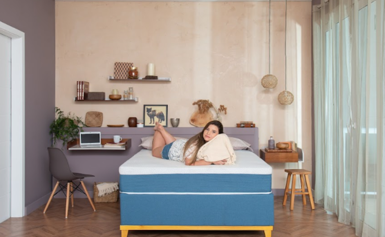 mulher deitada em um quarto aconchegante com cama, travesseiros, diversas plantas e outros itens decorativos é uma das dicas de como dormir bem.