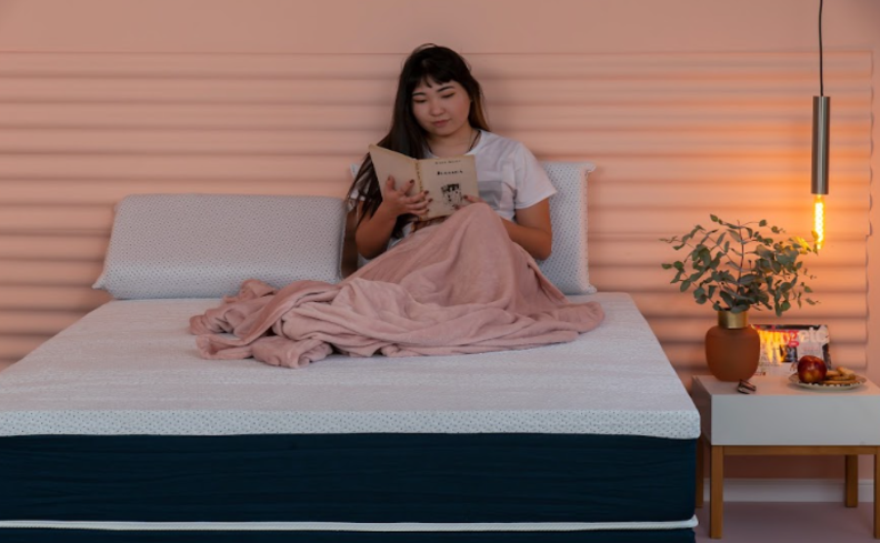 mulher sentada na cama com travesseiros e cobertor lendo um livro para saber para que serve melatonina.