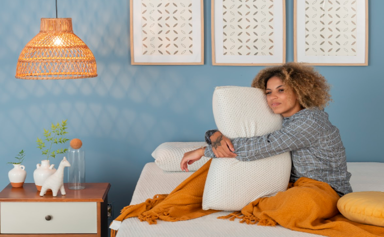 mulher sentada na cama abraçando um travesseiro pensando em qual é o hormônio do sono para conseguir ter noites de sono de mais qualidade.