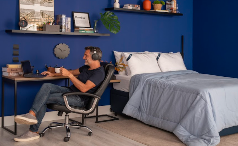 homem em um quarto sentado em uma cadeira de escritório segurando uma xícara de café pesquisando sobre quanto tempo dura o efeito da cafeína no corpo.
