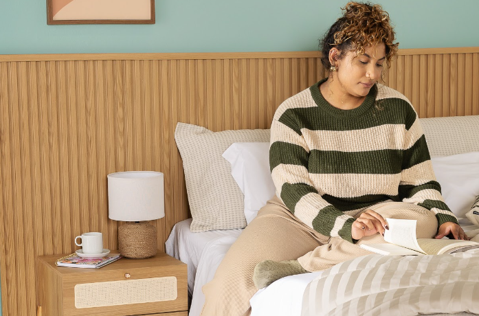 benefícios de ler todos os dias antes de dormir para ter boas noites de sono com uma mulher sentada na cama lendo um livro físico.