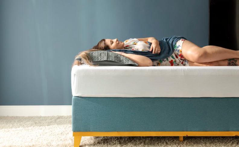 como dormir no calor sem ventilador com uma mulher deitada em uma cama com colchão, travesseiro e uma manta leve.