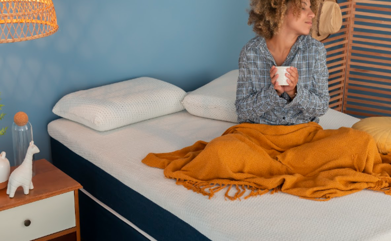 acordar cansado após dormir por muitas horas com uma mulher sentada na cama segurando uma caneca.