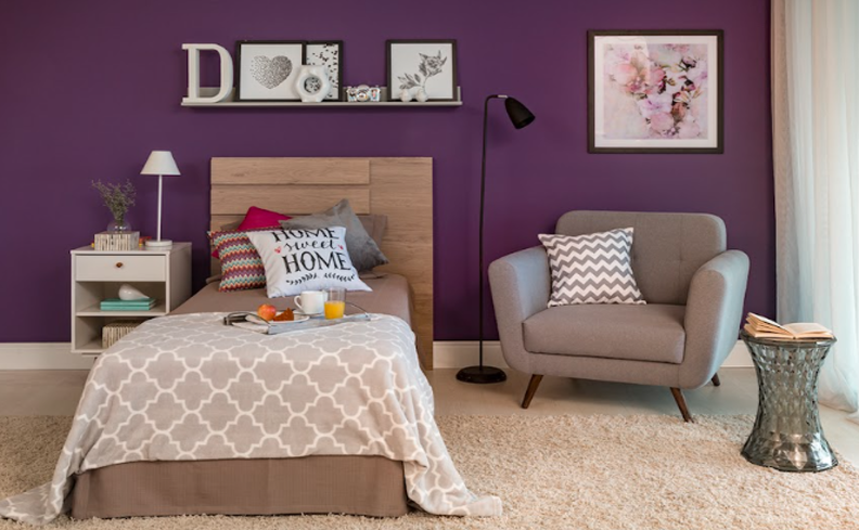 quarto de hóspedes e quarto de visitas com cama posta, poltrona, diversas almofadas, luminária de chão, quadros decorativos e mesas de apoio.