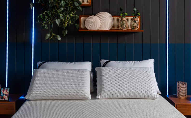 dicas de como lavar um travesseiro, em um quarto com paredes azuis, led, prateleiras com diversos itens decorativos e quatro travesseiros na cama.