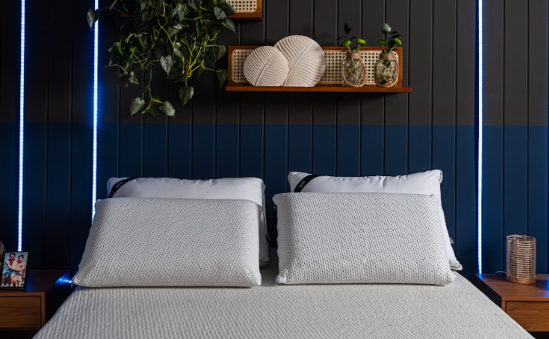 melhor colchão casal em um quarto com colchão de molas ensacadas, quatro travesseiros, parede azul e duas mesas de cabeceira.