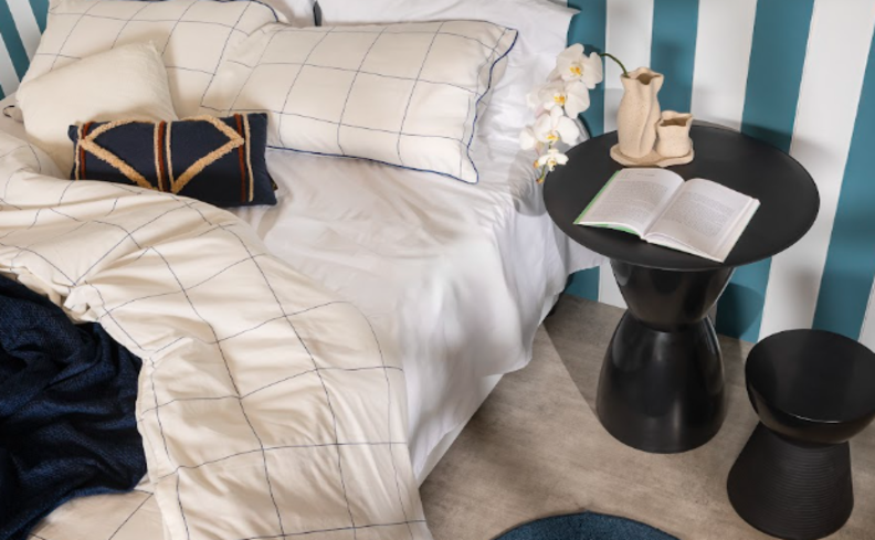 qualidade do sono com um quarto confortável com roupa de cama branca, travesseiros, mesa de cabeceira, tapete, vaso com plantas e um livro.