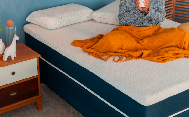 como fazer para dormir rápido com uma mulher sentada no colchão segurando uma xícara de chá tentando pegar no sono.