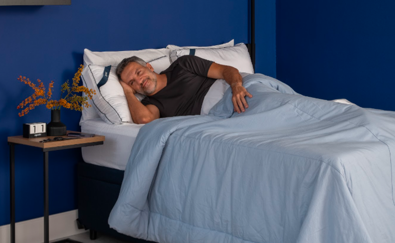 a importância de ter uma boa qualidade do sono com um homem deitado em uma cama no quarto com edredom azul, mesa de cabeceira e parede azul.
