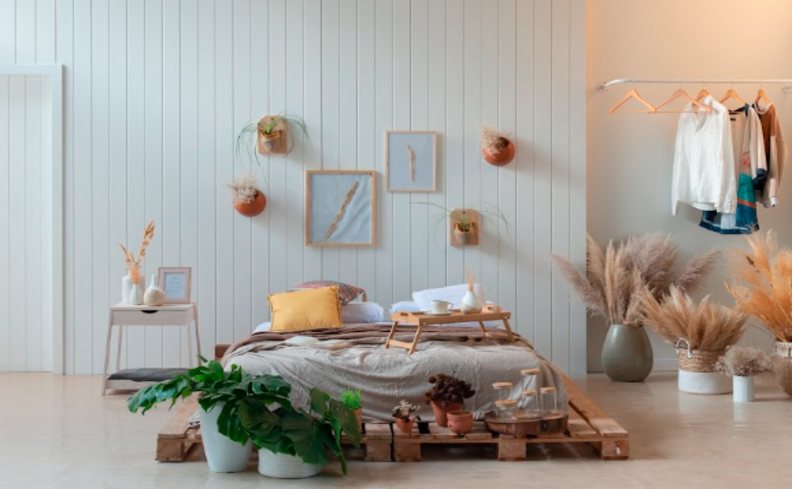 melhor colchão para coluna, em um quarto com colchão no chão, mesa de cabeceira, arara de roupas e diversos vasos com plantas e flores.