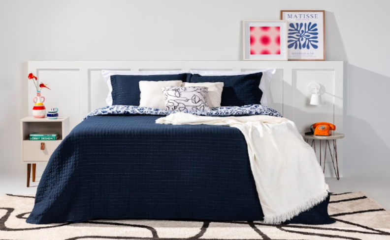 posição para dormir na gravidez em um quarto com colchão, roupas de cama em azul e branco, mesas de cabeceira, quadros decorativos, tapete e itens decorativos para deixar o ambiente mais aconchegante e bonito.