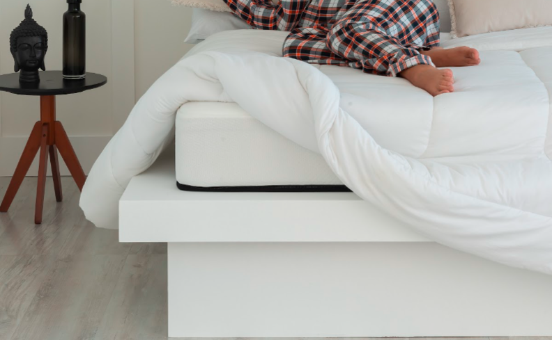 tempo ideal de sono profundo com uma mulher deitada na cama em um quarto com roupas de cama brancas e mesa de cabeceira preta com dois vasos decorativos.
