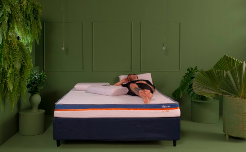 saiba o que é mola ensacada para dormir melhor. homem deitado em uma cama com colchão Guldi e três travesseiros em um quarto com paredes verdes e diversas plantas.