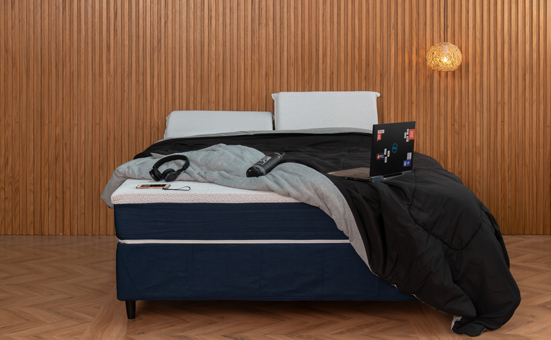 dicas para trocar um colchão velho, quarto com base box de cama com colchão, edredom preto, dois travesseiros e notebook em cima da cama.