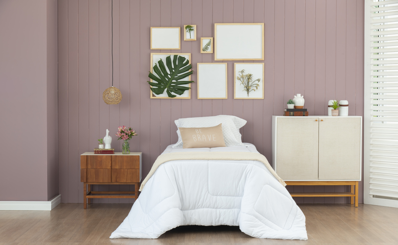 qual colchão comprar no quarto com colchão de solteiro, edredom branco, mesa de cabeceira, lustre pendente, cômoda com duas portas e diversos quadros decorativos na parede.