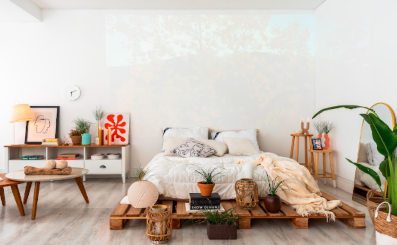 dicas para saber como dormir bem a noite toda em um quarto com um colchão em um estrado, roupas de cama confortáveis e travesseiro. Além de diversos itens decorativos.