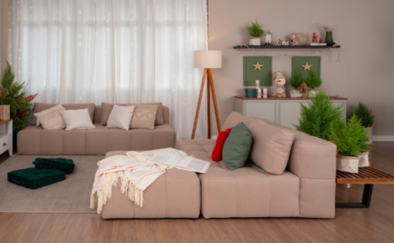 modelo e sofá moderno na sala de estar com diversos módulos do sofá bege, além de manta de sofá e diversas almofadas.