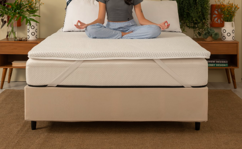 o que é sono reparador com uma mulher meditando sentada em um colchão com pillow top, além de duas mesas de cabeceira e vasos com plantas.