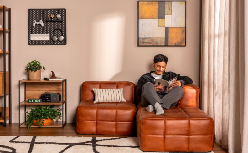 homem lendo um livro sentado em um sofá de espuma a vácuo da Guldi em uma sala de estar com tapete, mesa lateral e diversos itens decorativos no ambiente.