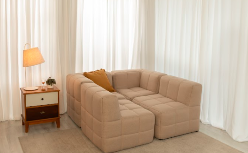 sofá em módulos formando uma cama pequena na sala de estar com tapete, mesa lateral, luminária de mesa e almofada.