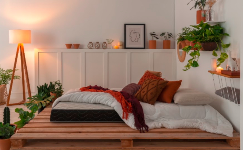 dicas para ter uma boa noite de sono com aromaterapia com cama em um pallet no quarto com roupa de cama branca, almofadas, luminária de chão e diversos itens de decoração.
